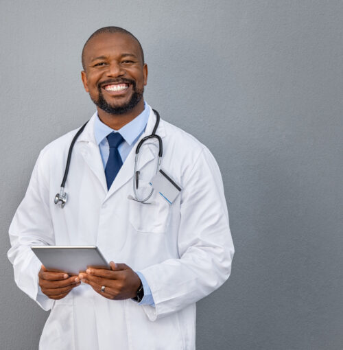 Smiling doctor standing on grey wall African american doctor holding digital tablet against grey background. Smiling mature doctor in labcoat standing against gray background. Successful happy healthcare worker looking at camera, copy space.