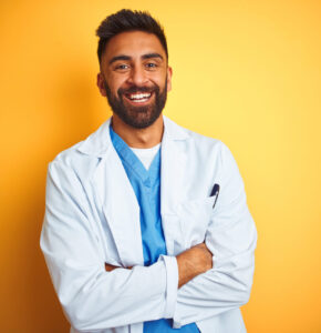 Young indian doctor man standing over isolated yellow background happy face smiling with crossed arms looking at the camera. Positive person. Young indian doctor man standing over isolated yellow background happy face smiling with crossed arms looking at the camera. Positive person.